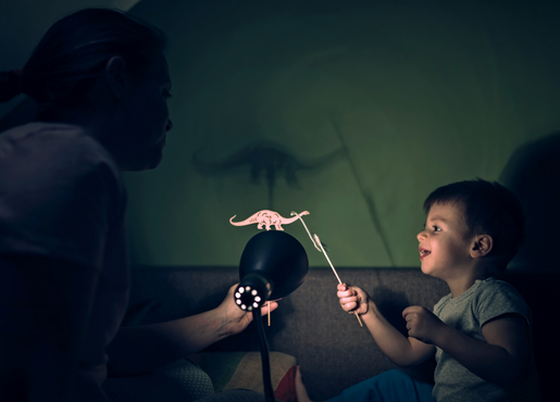 young boy making shadow puppets with parent in a dark room. 