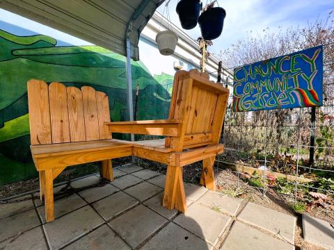 A friendship bench sits outside of the Chauncey Public Library, beside a Blessing Box and a community garden.