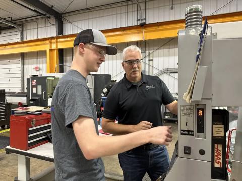 Hess Industries founder Mark Hess quizzes apprentice Tyler Duckworth on his knowledge of a CNC machine.