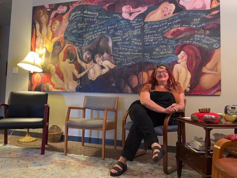 Christine Wilson, executive director of Women Writing for (a) Change, sits underneath a painting donated by a former student of the program.